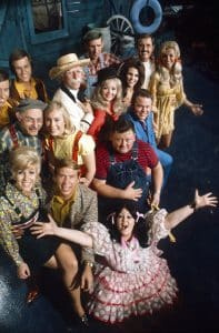   HEE HAW, viršuje, iš kairės: Jimas Hageris, Jonas Hageris (Hager Twins), Gordie Tapp (kepurė), Stringbean (David Akeman, viršuje, centre), Archie Campbell (ūsai), Gunilla Hutton, vidurinė eilė, iš kairės: Senelis Jonesas (Louis Marshall Jones), Cathy Baker, Jeannine Riley (juoda skrybėlė), Junior Samples (juostelės), Lisa Todd, Roy Clark (mėlynas kostiumas), priekyje, iš kairės: Mary Taylor, Buck Owens, Lulu Roman